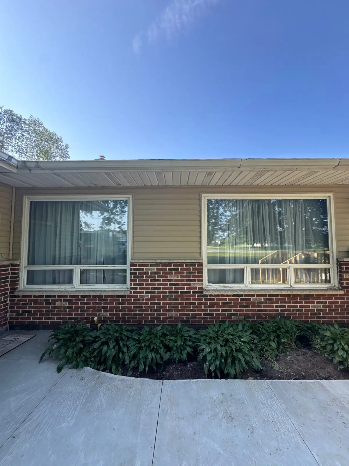 Gutter run along the eave of a ranch home above two new picture windows