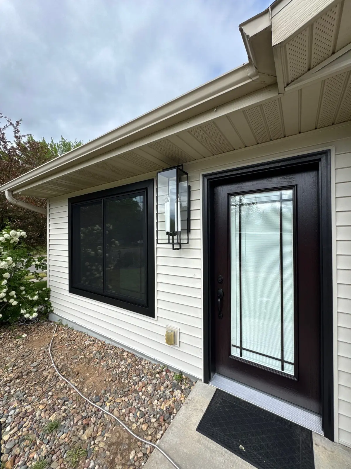 New black framed window and black entry door installed on a white sided home
